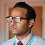 Close-up portrait of a serious man wearing glasses and tie indoors.